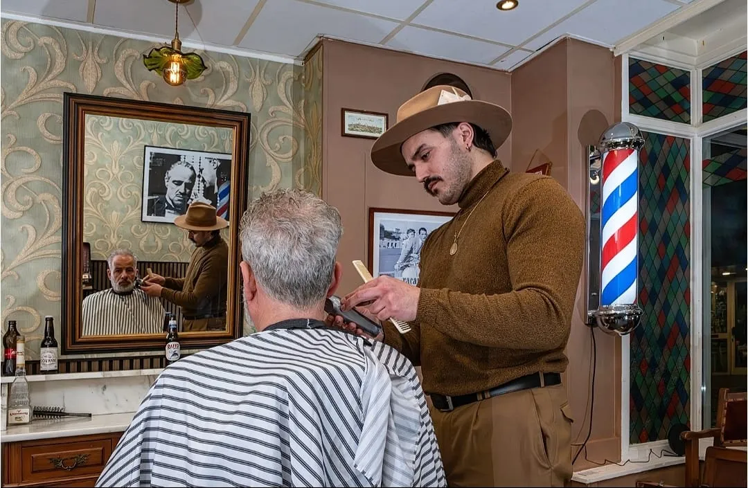Stefano aan het werk bij The Italian Barber, met op de achtergrond de barber pole en de vergulde spiegel